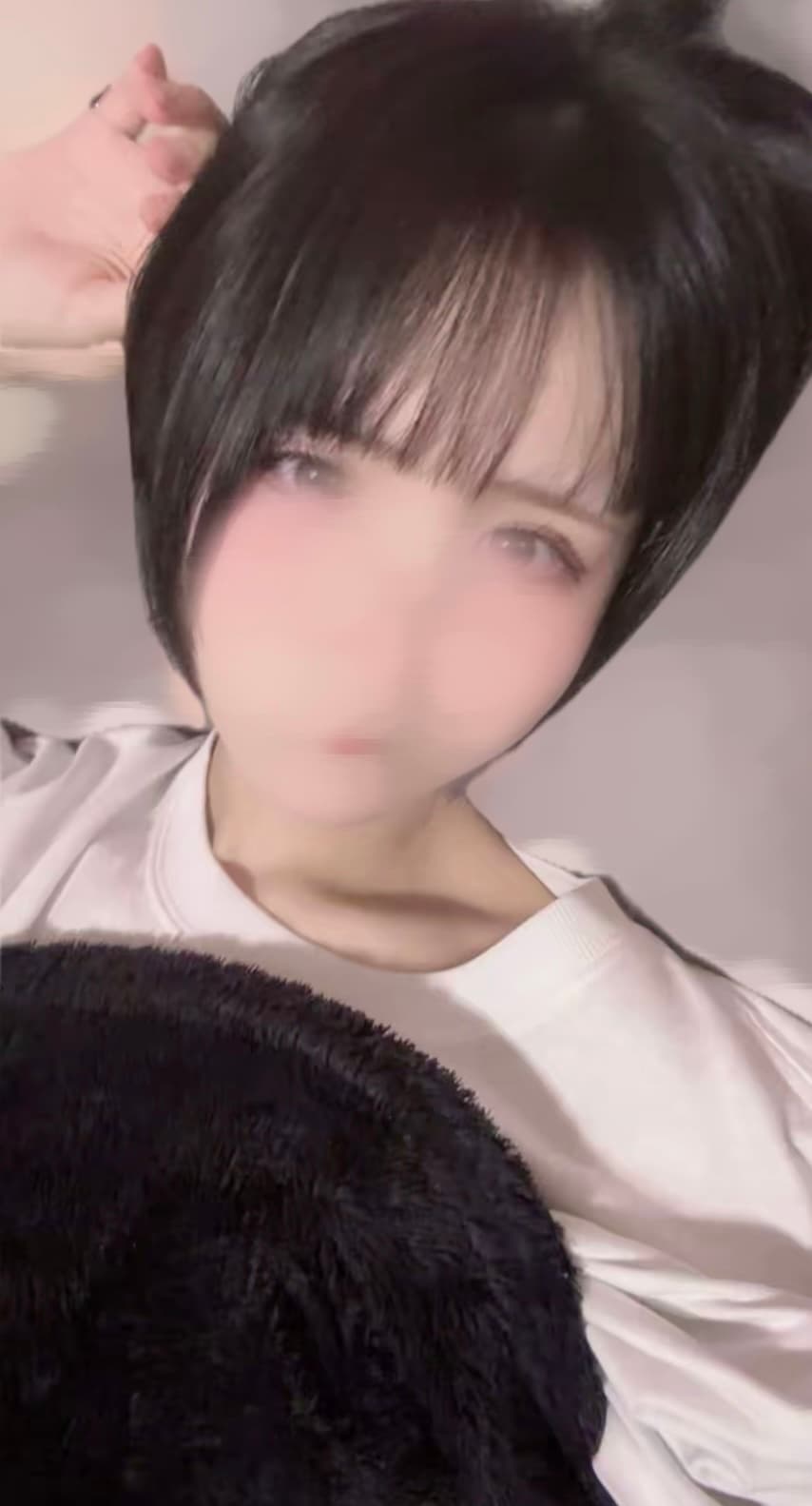 かなが白いTシャツを着て微笑み、柔らかな背景に座っています。