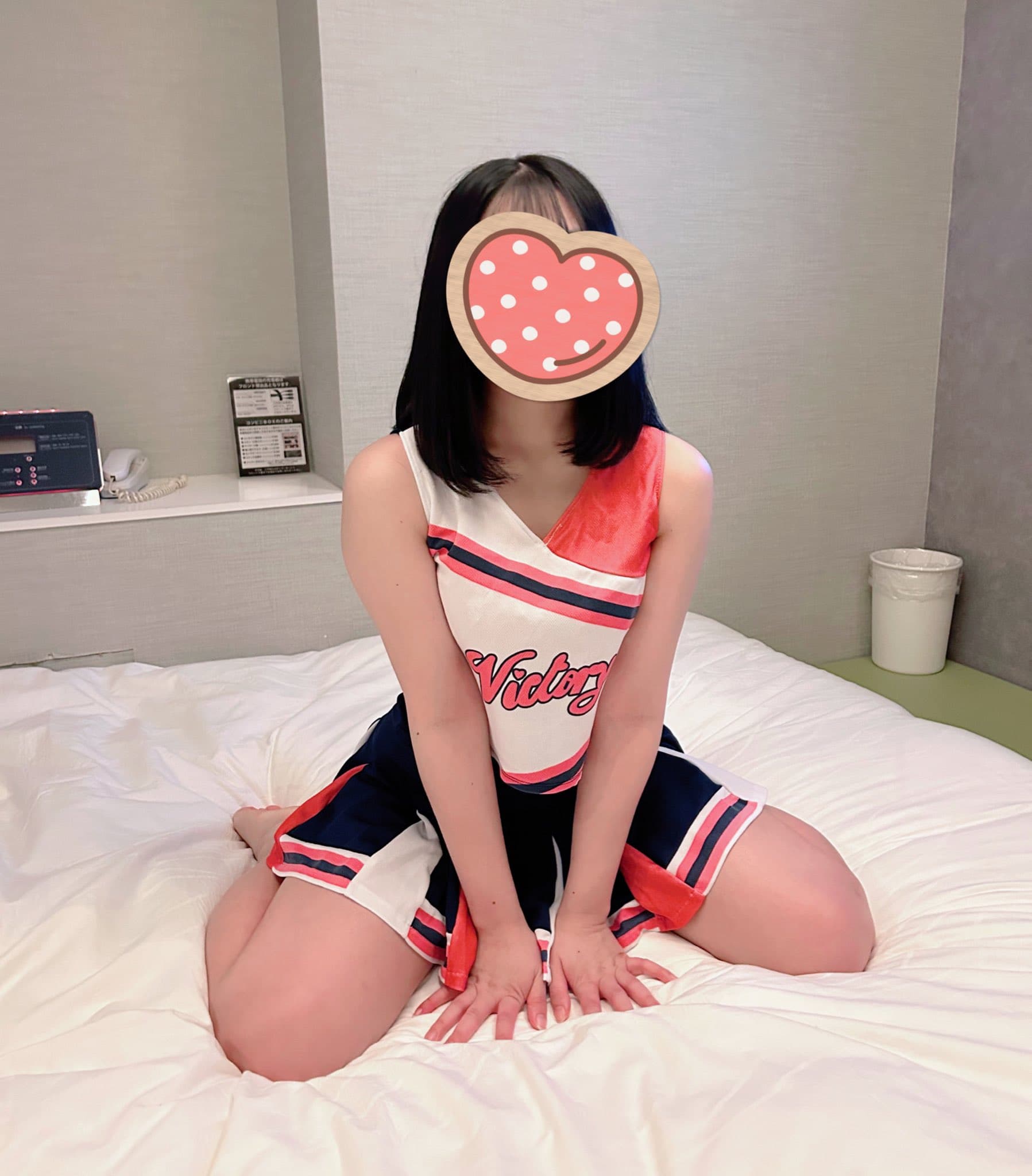 りりがベッドの上で可愛らしいチアリーダーの衣装を着て座っている。