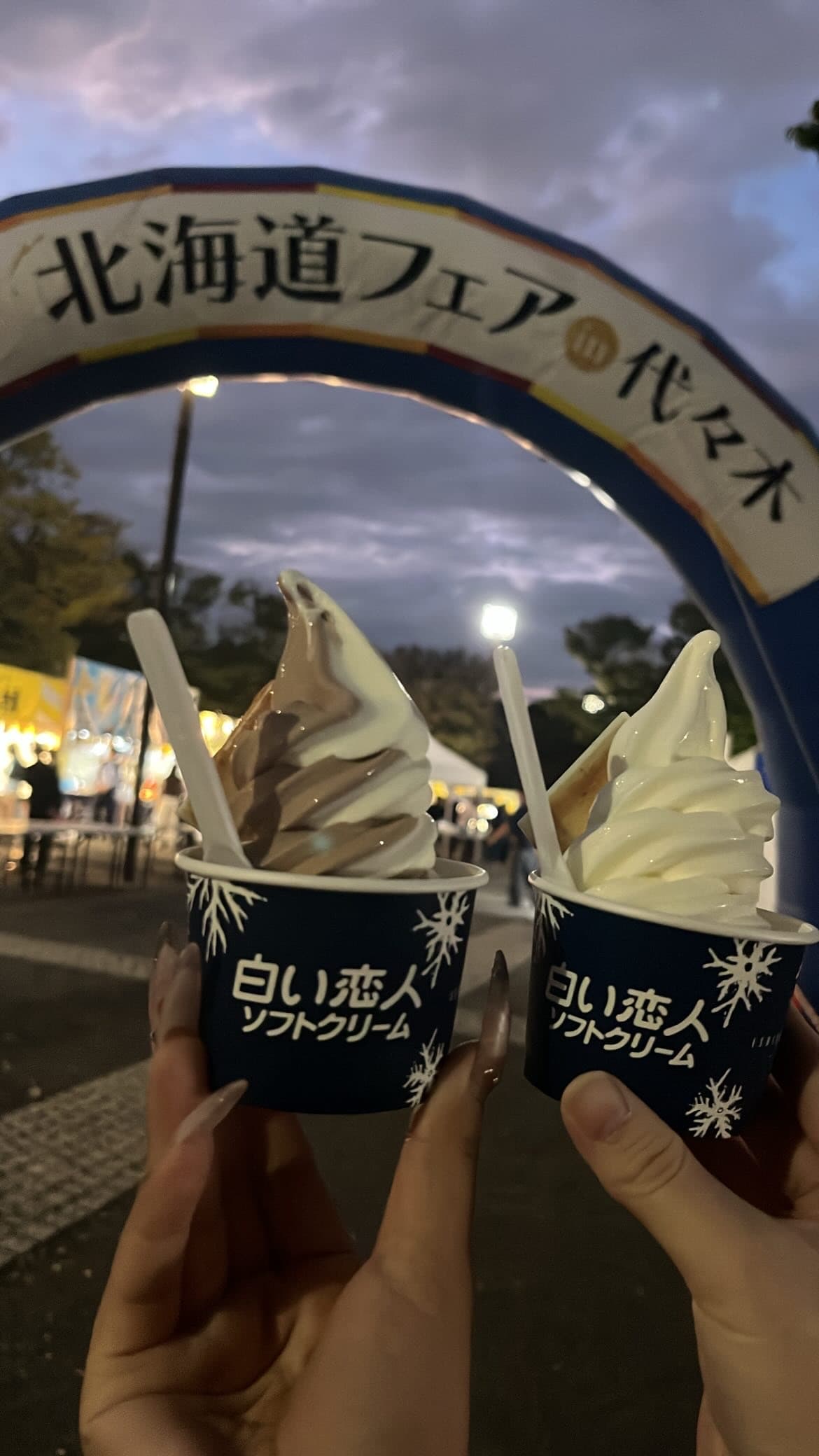 せいらが夕暮れのフェアでソフトクリームを持って微笑む。