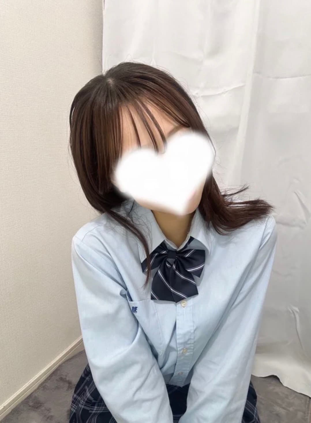 まきが青いシャツとネクタイを着て微笑んでいる。背景は白い布。