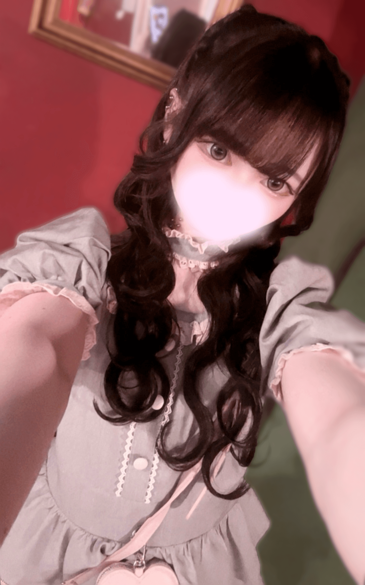 さとは、可愛らしいグリーンのドレスを着て微笑み、背景には赤い壁がある。