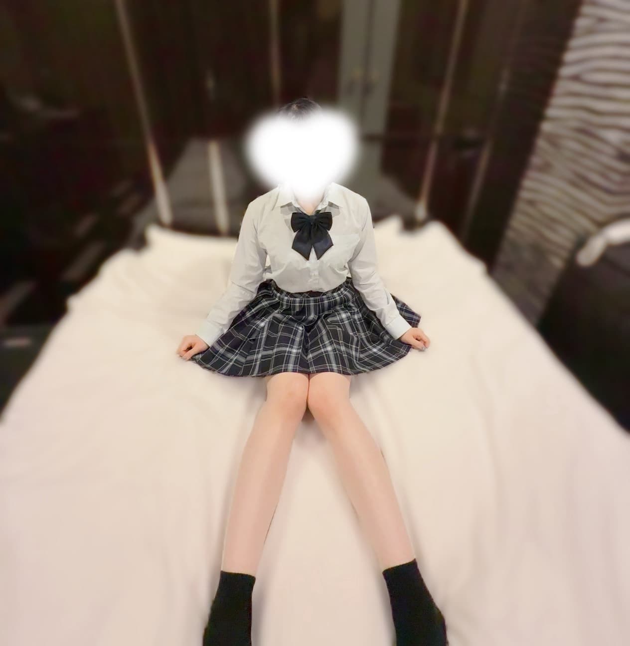 ほの(JK上がりたて18歳)がベッドに座り、制服姿で微笑んでいる。