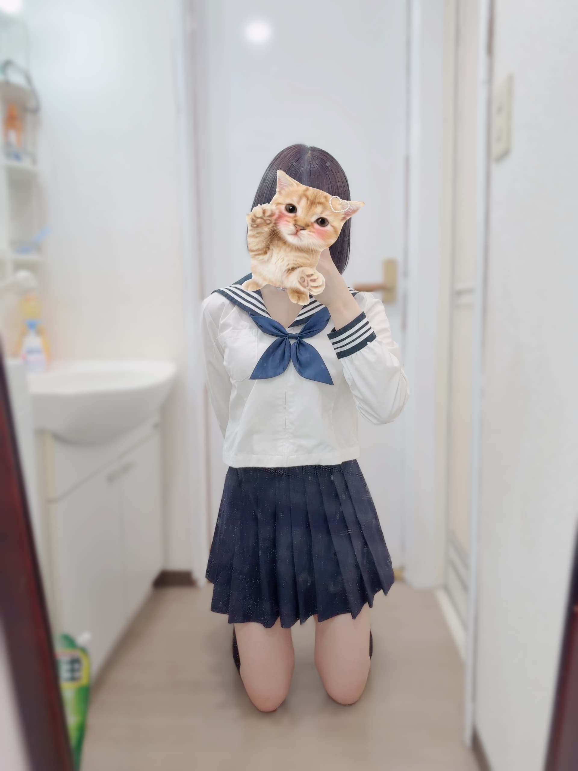 ほの(JK上がりたて18歳)がセーラー服姿で鏡の前に kneelし、猫を抱えて微笑む。